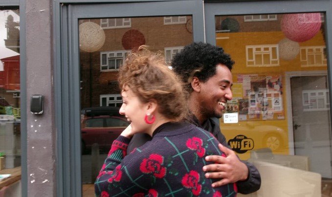 Two people smile and hug outside a community centre
