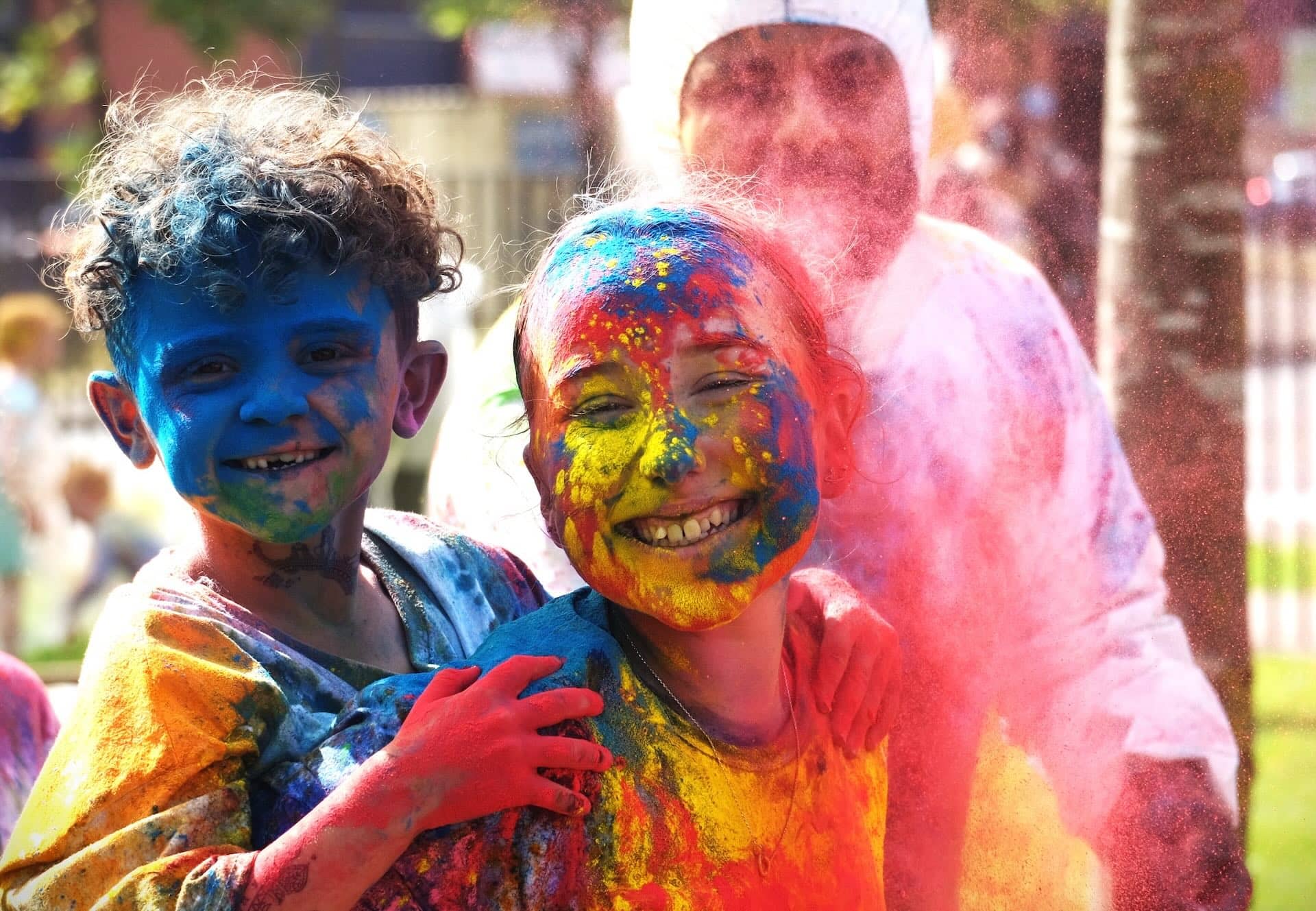 The image shows two people covered in colorful powders, smiling and celebrating. This scene is likely from a festival like Holi, where participants throw colored powders to celebrate joy and togetherness.