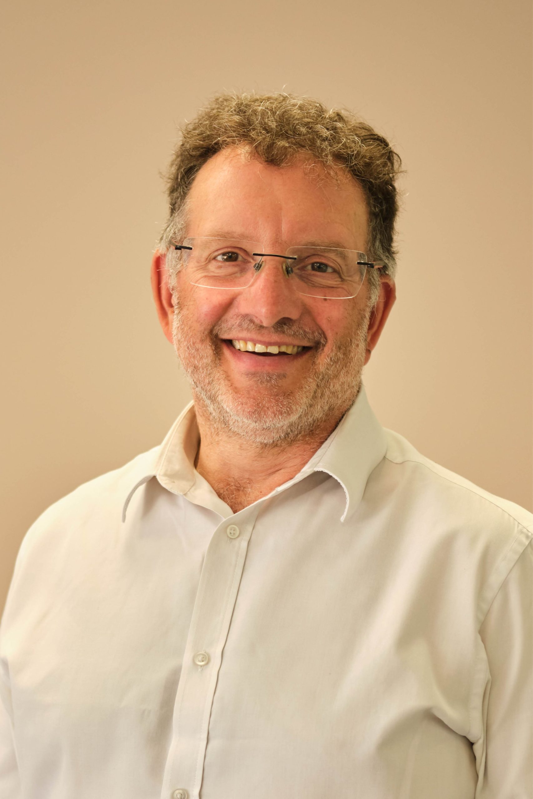 The image shows a smiling man with glasses wearing a light-colored button-up shirt against a plain background.