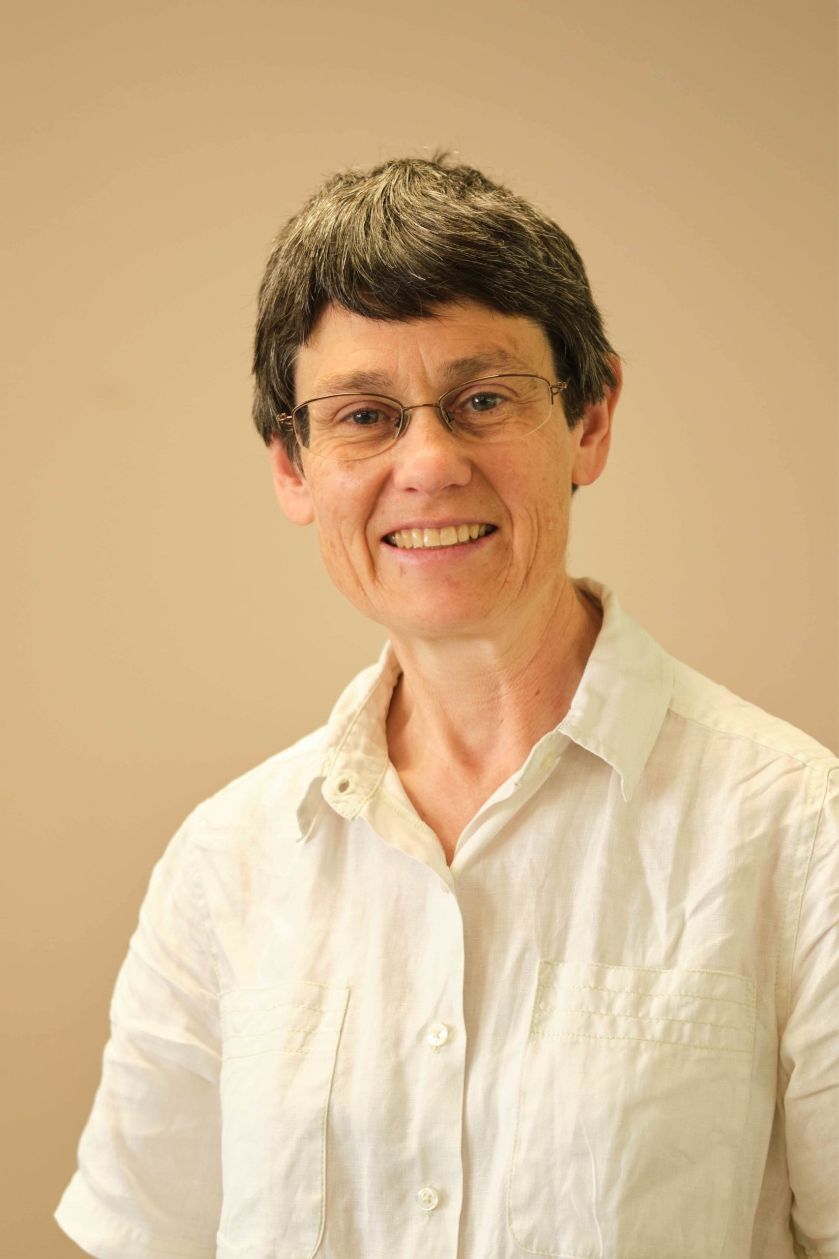 The image shows a person with short hair and glasses, wearing a light-colored, button-up shirt. The background is plain.