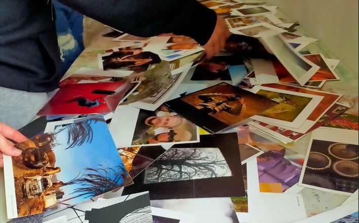 Two hands sort through a pile of colourful photographs on a table