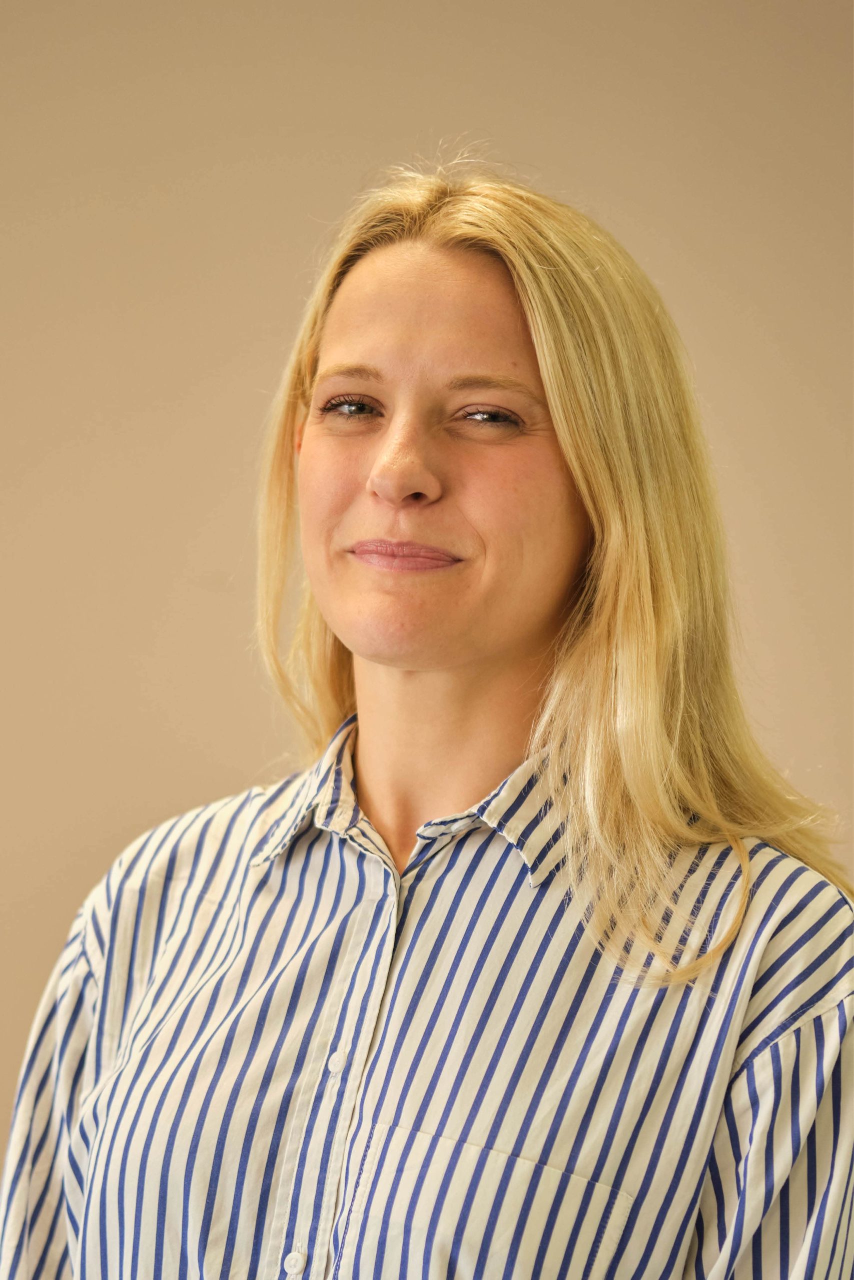 The image shows a person with long blonde hair wearing a blue and white striped shirt. The background is plain and light-colored.