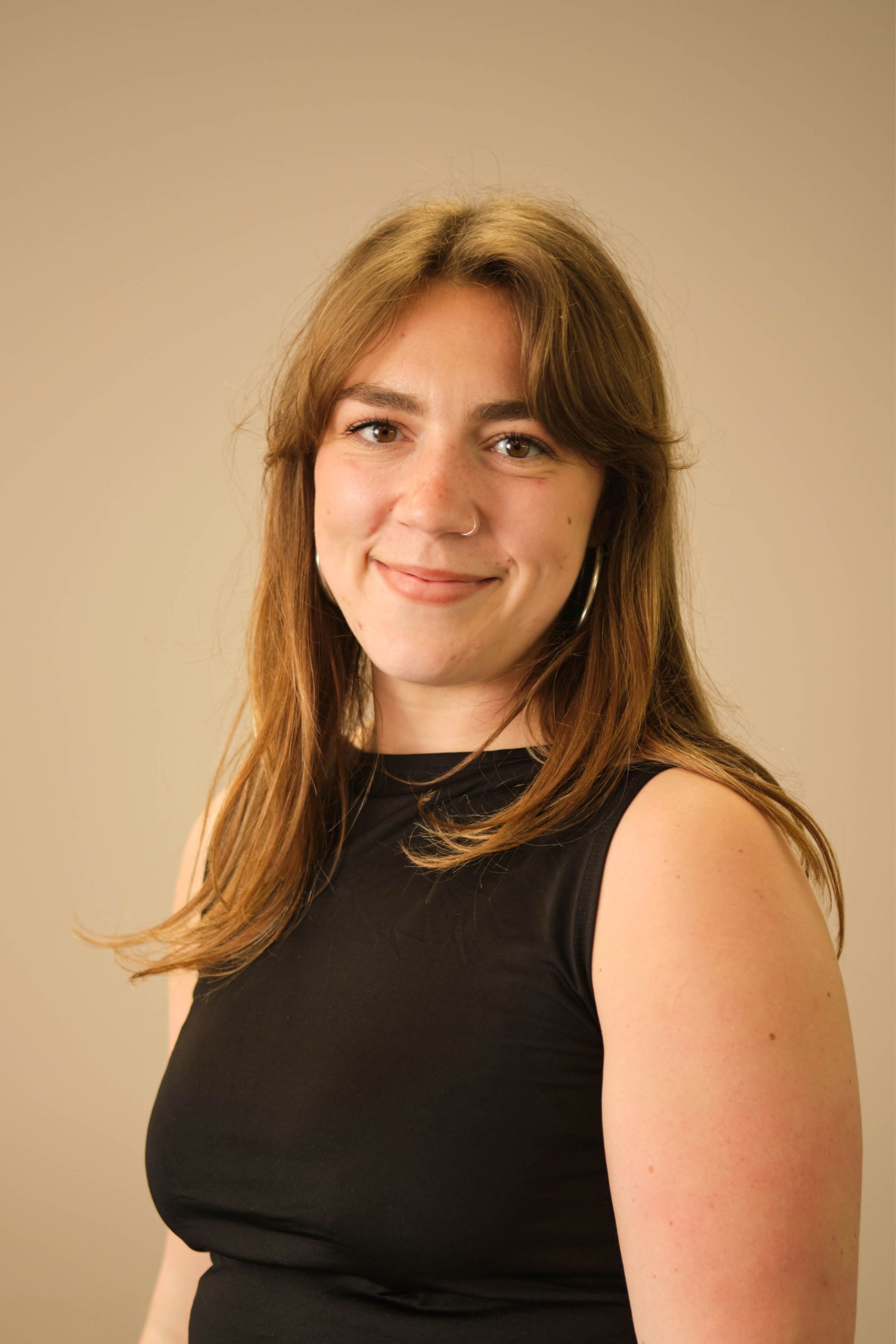 The image shows a person with long hair, wearing a black sleeveless top, and smiling. The background is plain and neutral.