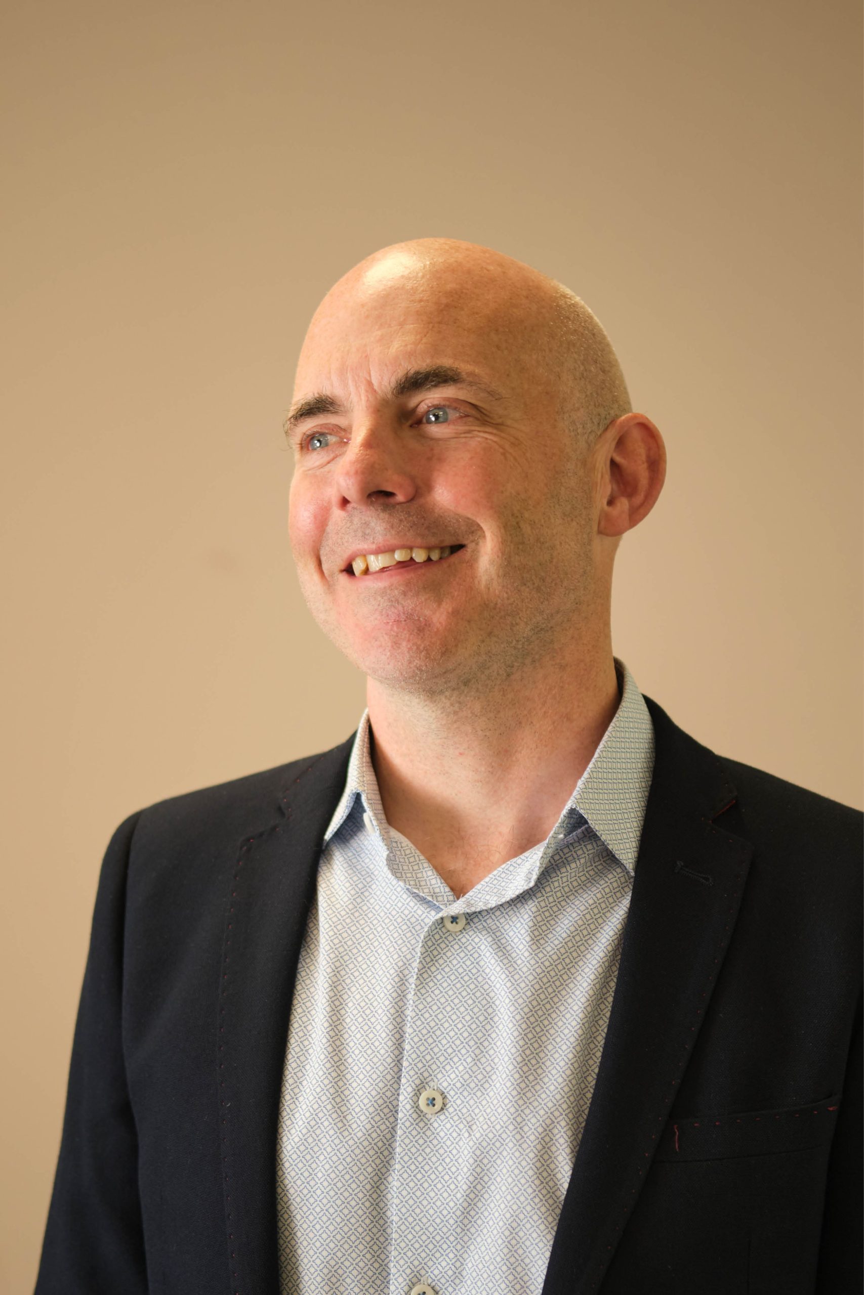 This image shows a person wearing a suit jacket and dress shirt, smiling and looking off to the side.