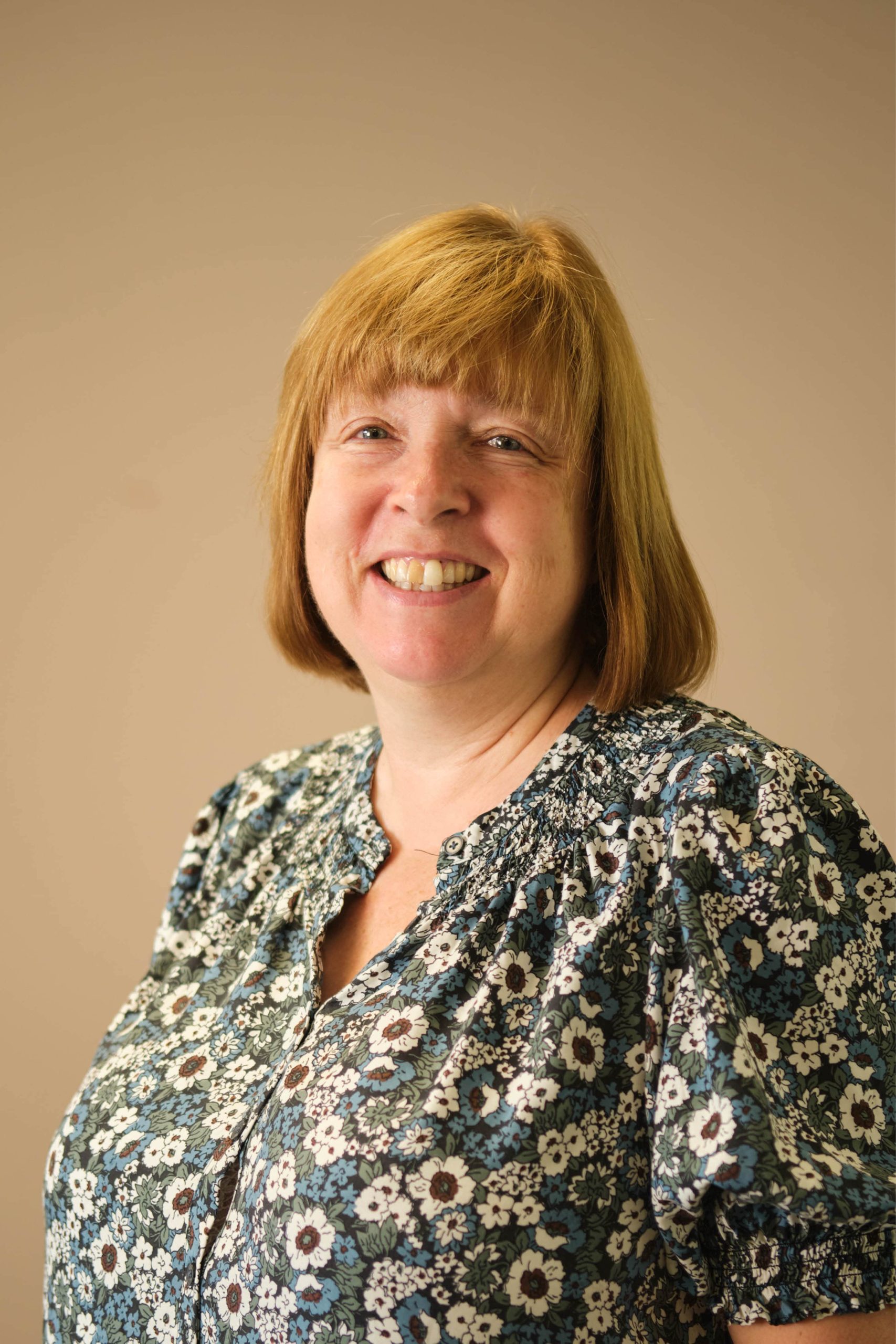 The image shows a person smiling, wearing a floral-patterned blouse. The background is a neutral color.