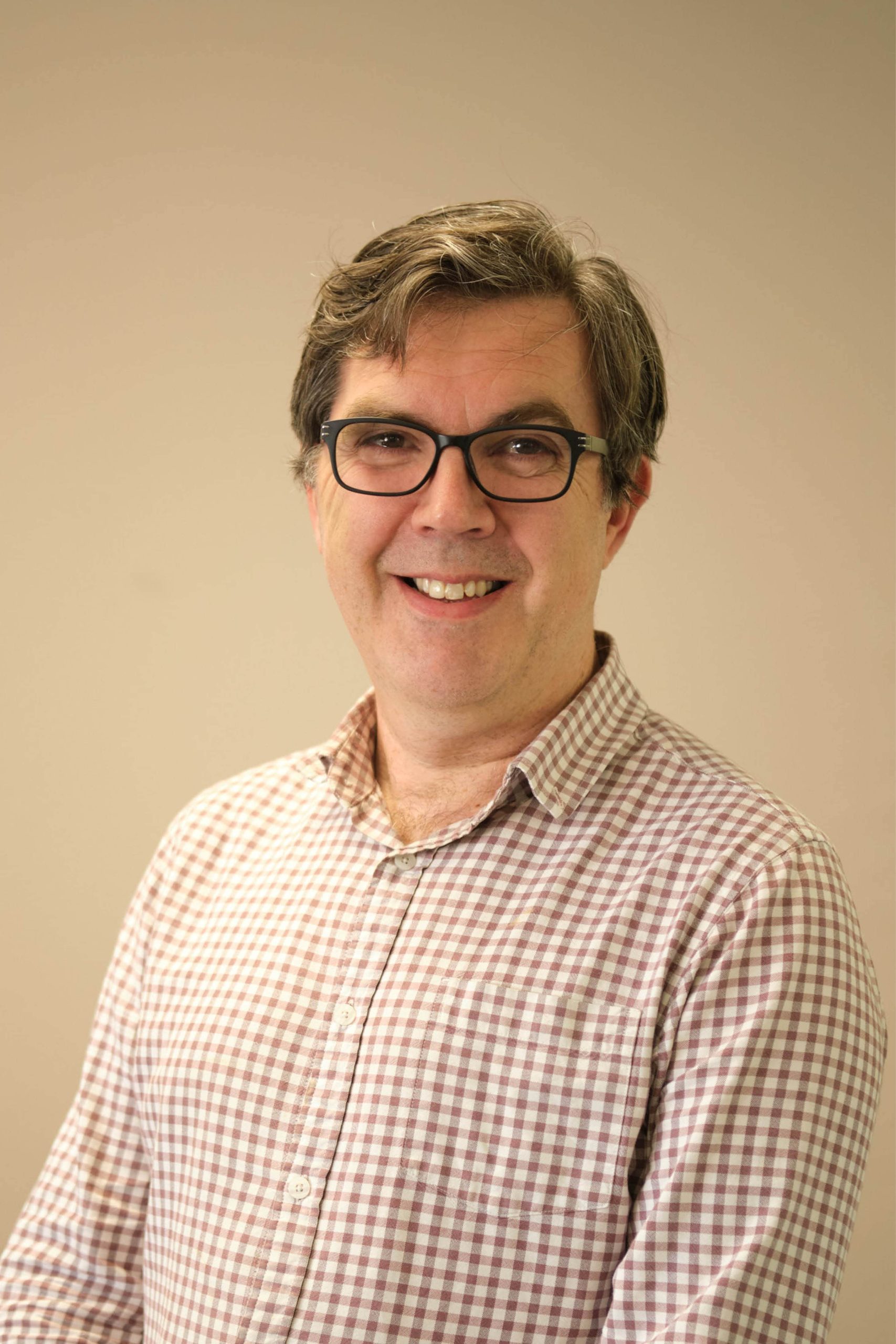 The image shows a person wearing glasses and a checked shirt, smiling at the camera.